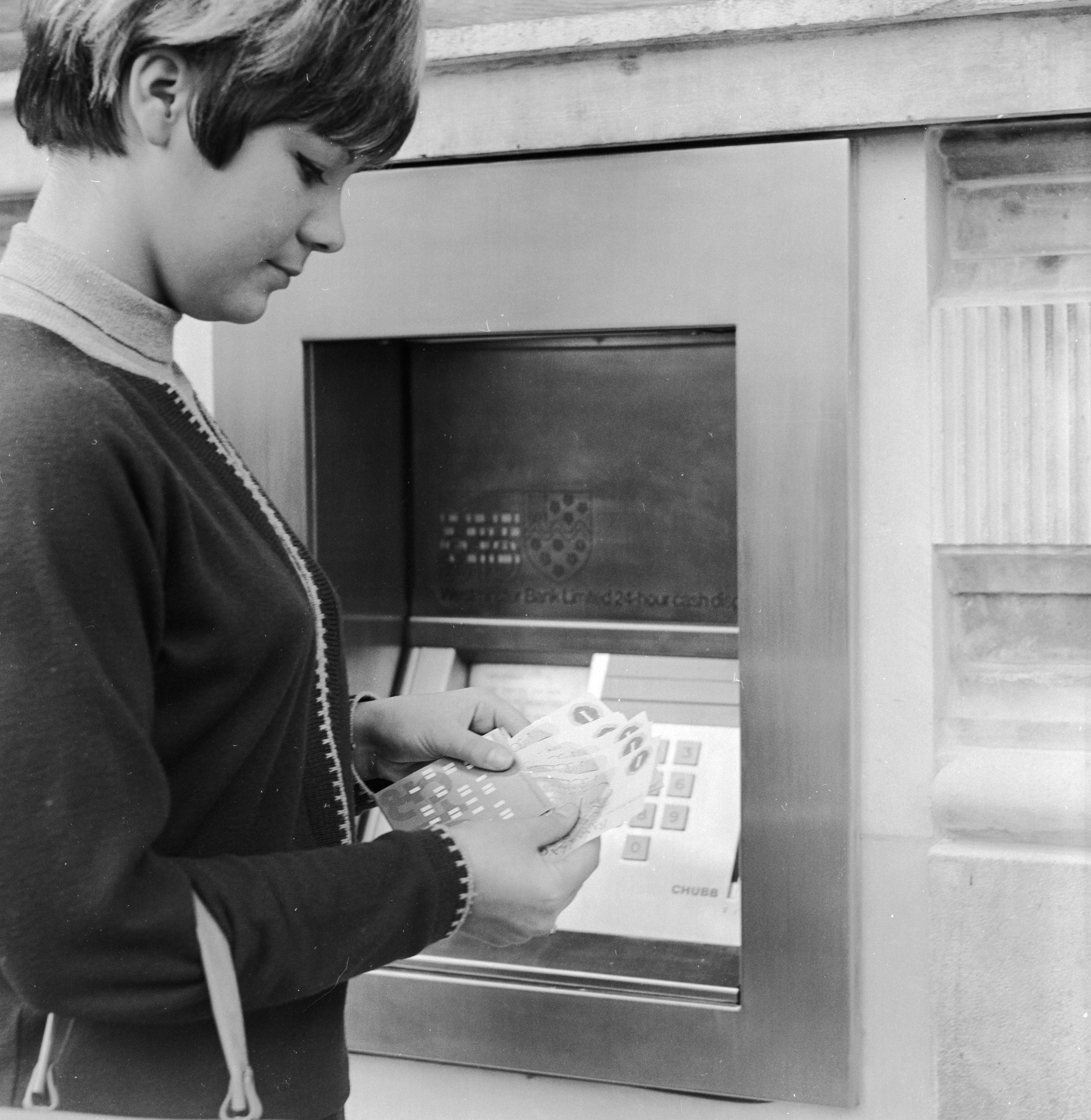 A customer counting out her money after using the world’s first cashpoint machine at a London ban